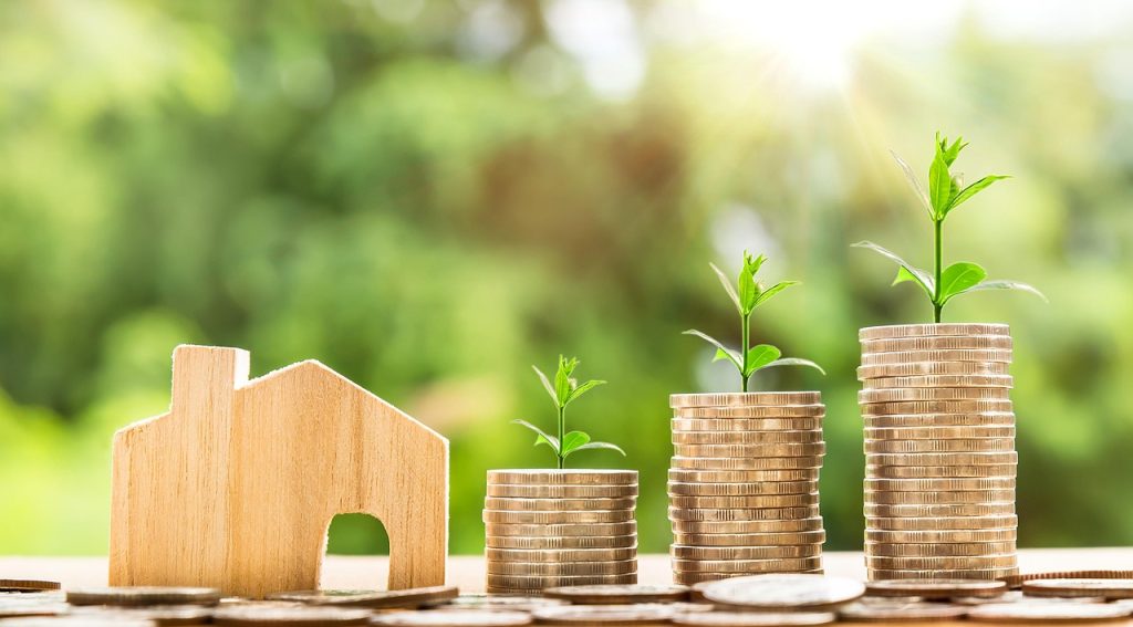 Drewniany domek i rosnące stosy monet.