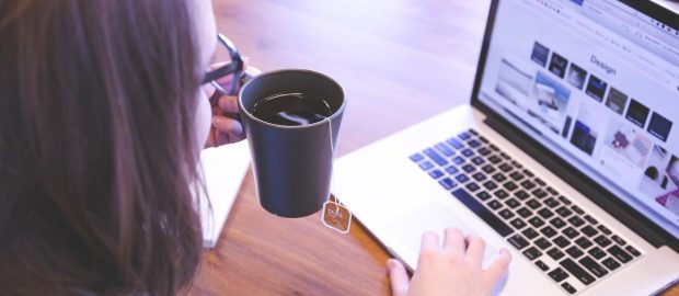 Osoba sprawdza konto bankowe na laptopie, trzymając kubek kawy.