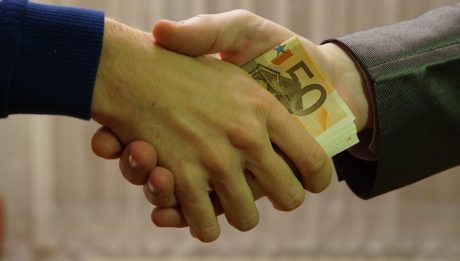 Uścisk dłoni z przekazywanym banknotem.